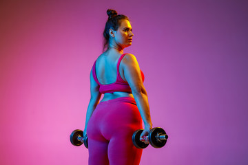 Young caucasian plus size female model's doing exercises on gradient purple background in neon...