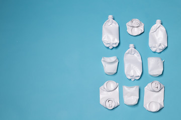 Crumpled plastic and metal cans lie on a blue background with copy space. Concept of littering of the environment and non-rotting waste.