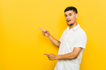 Young hispanic man excited pointing with forefingers away.
