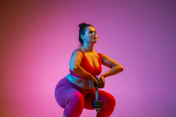 Young caucasian plus size female model's doing exercises on gradient purple background in neon light. Training in lunges with the weight. Concept of sport, healthy lifestyle, body positive, equality.