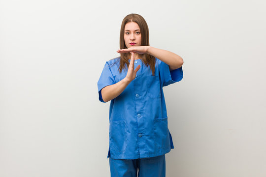 Young Nurse Woman Against A White Wall Showing A Timeout Gesture.