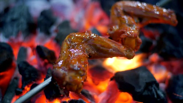 A roadside vendor is baking chicken wings on a coal furnace. 