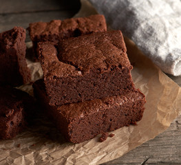 stack of baked square pieces of chocolate brownie cake on brown parchment paper