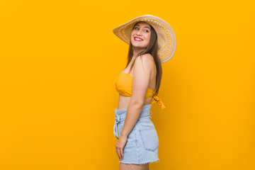 Young caucasian woman wearing a straw hat, summer look looks aside smiling, cheerful and pleasant.