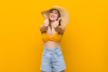 Young caucasian woman wearing a straw hat, summer look with thumbs ups, cheers about something, support and respect concept.