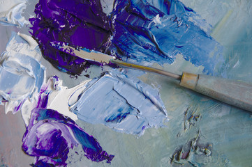 Artist's palette with blue and red oil paints with a bristle brush and a palette knife.