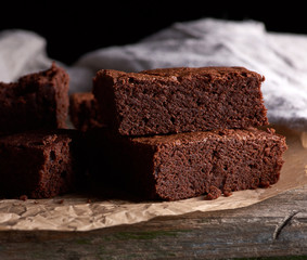 stack of baked square pieces of chocolate brownie cake on brown parchment paper