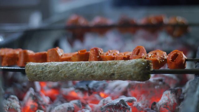 Camera panning close up of mutton seekh kebab being cooked over a furnace. 