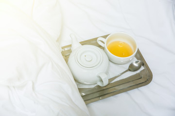 Tea cup and kettle on the tray. Morning at the hotel. White linen sheets.