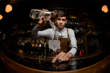 Young bartender pours cocktail from the jar