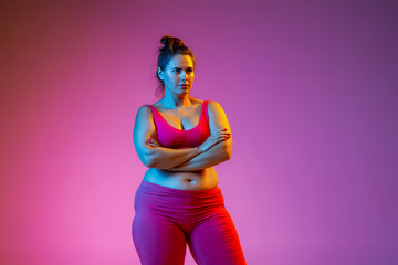 Young caucasian plus size female model's doing exercises on gradient purple background in neon...