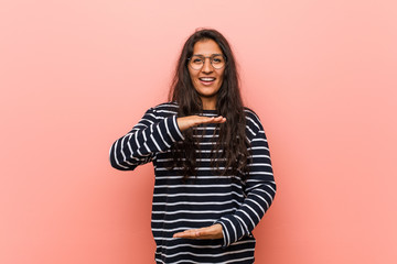 Obraz premium Young intellectual indian woman holding something with both hands, product presentation.
