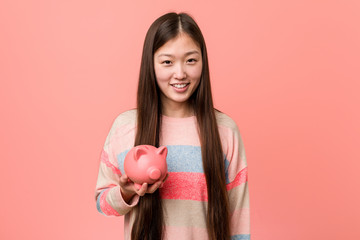 Obraz na płótnie Canvas Young asian woman holding a piggy bank happy, smiling and cheerful.
