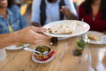 leisure, food and people concept - group of happy international friends eating at restaurant and male hand holding plate with chapati bread