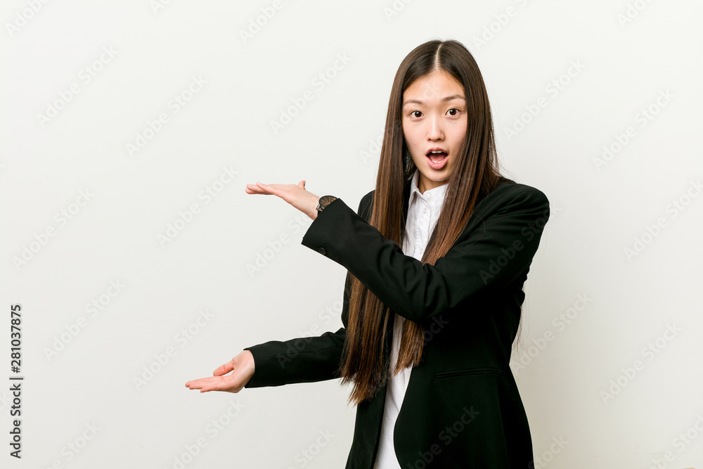 Wall mural young pretty chinese business woman shocked and amazed holding a copy space between hands.