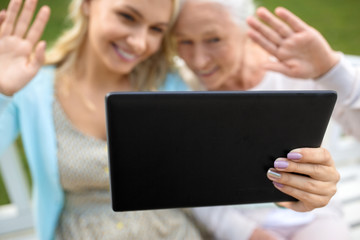 family, technology and people concept - close up of happy smiling adult daughter with tablet pc computer and senior mother on park bench waving hands