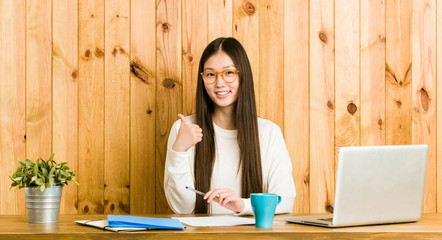 Young chinese woman studying on her desk smiling and raising thumb up