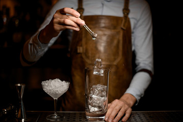 Bartender adds ice in cocktail glass with tongs