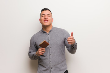 Young latin man holding a wallet smiling and raising thumb up