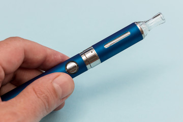 Hand holding vape pen metal electronic cigarette with vaping blue background