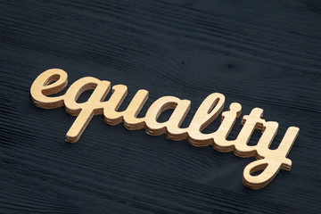 EQUALITY word carved out of plywood. Symbol of gender equality. Black wooden background.