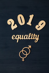 EQUALITY word carved out of plywood. Symbol of gender equality. Black wooden background.2019