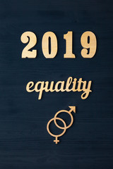 EQUALITY word carved out of plywood. Symbol of gender equality. Black wooden background.2019