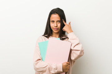 Fototapeta premium Young hispanic woman holding some notebooks pointing his temple with finger, thinking, focused on a task.