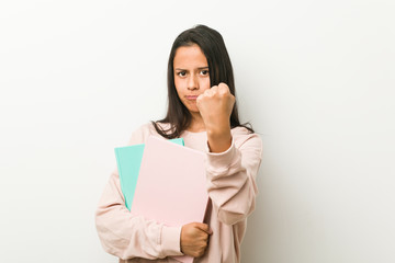 Naklejka premium Young hispanic woman holding some notebooks showing fist to camera, aggressive facial expression.