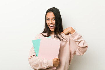 Naklejka premium Young hispanic woman holding some notebooks surprised pointing at himself, smiling broadly.