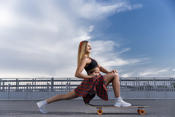 Fototapeta premium Young stylish woman performs stretching and rides a skateboard while listening to music.