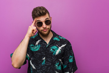 Young man wearing a vacation look pointing temple with finger, thinking, focused on a task.