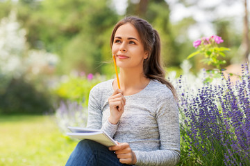 gardening and people concept - young woman writing to notebook at summer garden