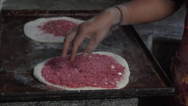 Side view of hands putting red power on round flat rolled dough then adding a dough lid (sv&aring;r d&ouml;pa, stor deg som &auml;r rund och utkavlad)
