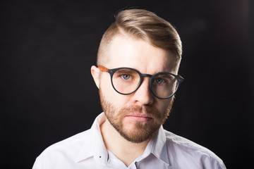 Portrait of young bearded man and in glasses over the black background