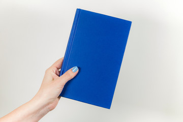 Closeup view of female hand holding blue book with hardback. Horizontal color photography.