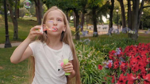 little girl blowing soap bubbles in summer park. Happy child kid outdoor portrait, cute happy schoolgirl