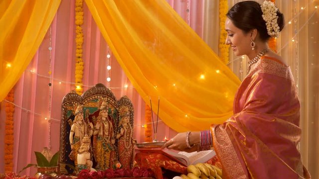 Indian woman in saree worshipping Ram Darbar / family idols at home - Puja Festival Celebration. Indian stock footage of traditional woman of Hindu family - Pooja ki thali with diya and incense sticks