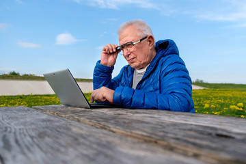 active old age, senior people and lifestyle concept - Elderly man 70-75 years old using laptop computer in summer park. Happy grandfather outdoors