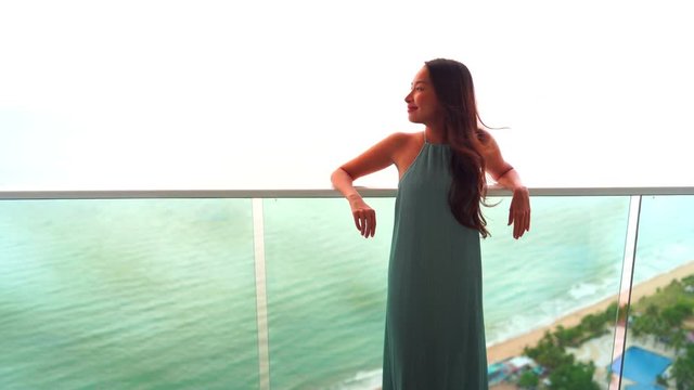 Attractive young woman leaning on the balcony of a luxury resort hotel looking out to sea
