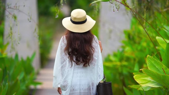 Attractive young woman in white summer dress and straw hat walkthrough a luxury Paradise
