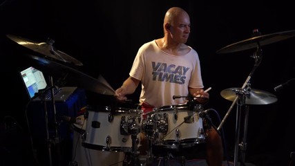 Medium shot of a drummer playing his drumkit while sweating a lot.