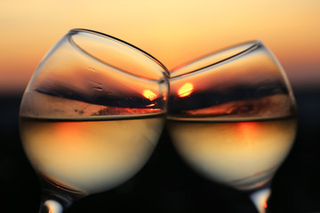Two glasses with white wine on sunset background, evening sun is reflected in a misted glass. Concept of celebration, romantic cocktail, love date, wine tasting