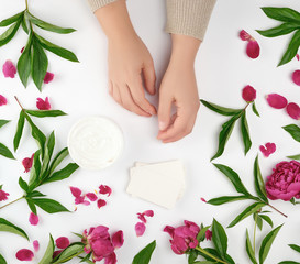 two female hands and a jar with thick cream and burgundy flowering peonies with green leaves