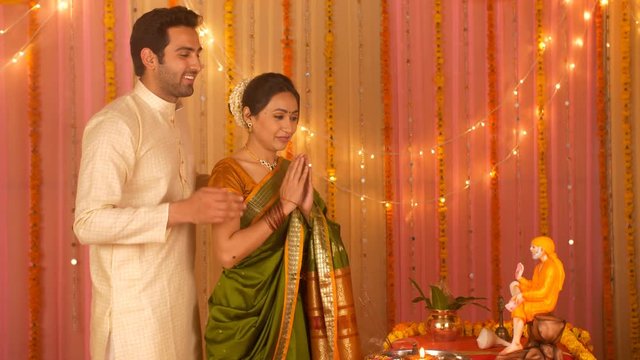 Indian married couple wearing ethnic clothes for Puja at home - Offering prayers to Sai Baba. Indian stock video of young married couple worshiping Hindu Preacher Sai Baba - Colorful festive backgr...