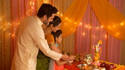 Happy Indian family performing Hindu rituals on the auspicious day of Janamashtmi. Indian stock footage of a nuclear family of husband  wife  and daughter worshiping Lord Krishna