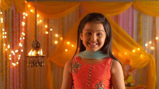 Indian girl with a smiling face looking at diyas - folding hands in namaskar position - Greeting pose. Indian stock video of a cute girl - getting prepared for Diwali Puja at home. Colorful festive...