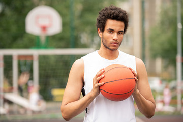 Young serious multicultural athlete holding ball for playing basketball
