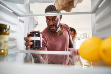 View Looking Out From Inside Of Refrigerator As Couple Open Door And Unpack Shopping Bag Of Food