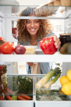 View Looking Out From Inside Of Refrigerator As Woman Opens Door And Unpacks Shopping Bag Of Food